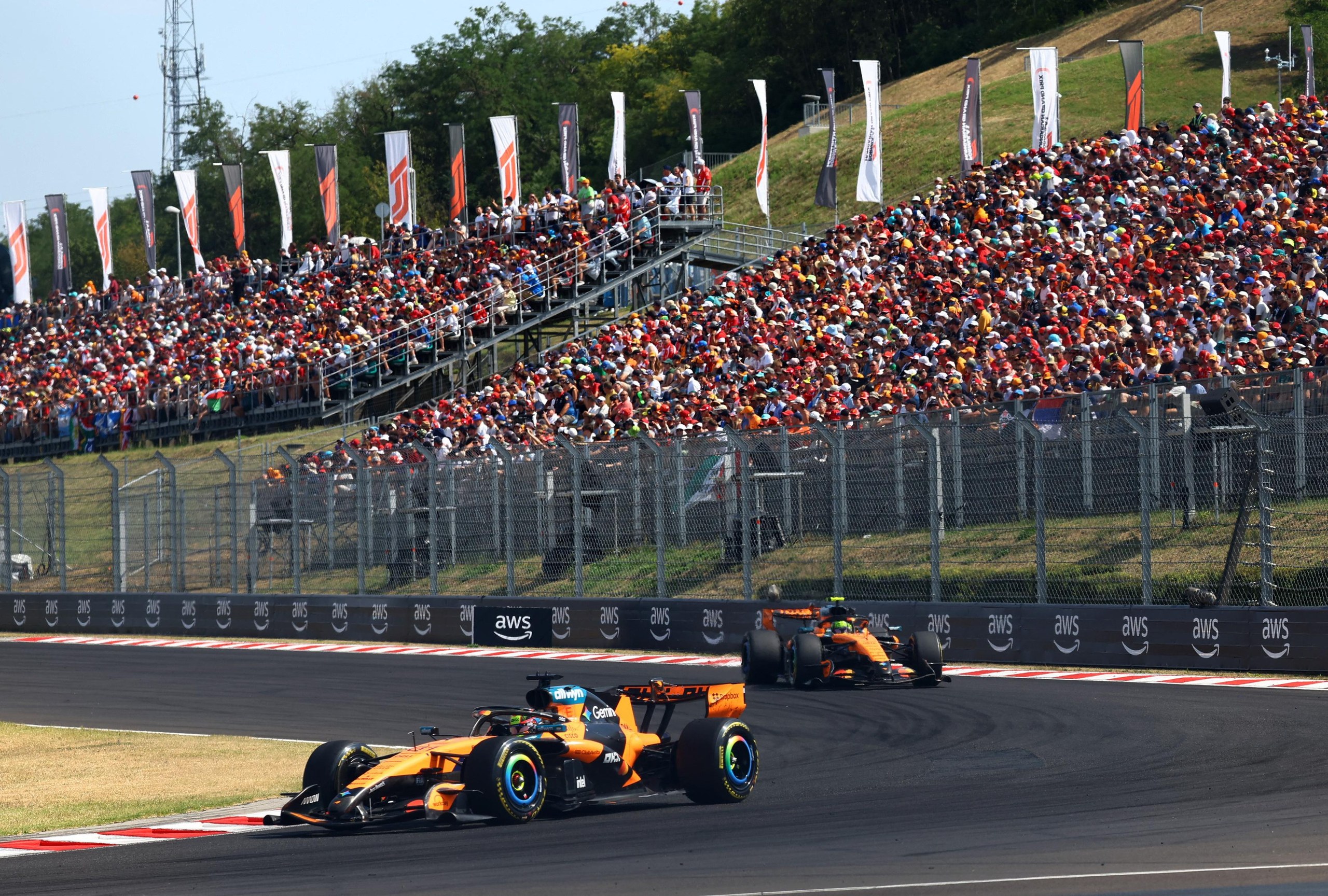 Oscar Piastri driving ahead of Lando Norris in front of a stand full of spectators.