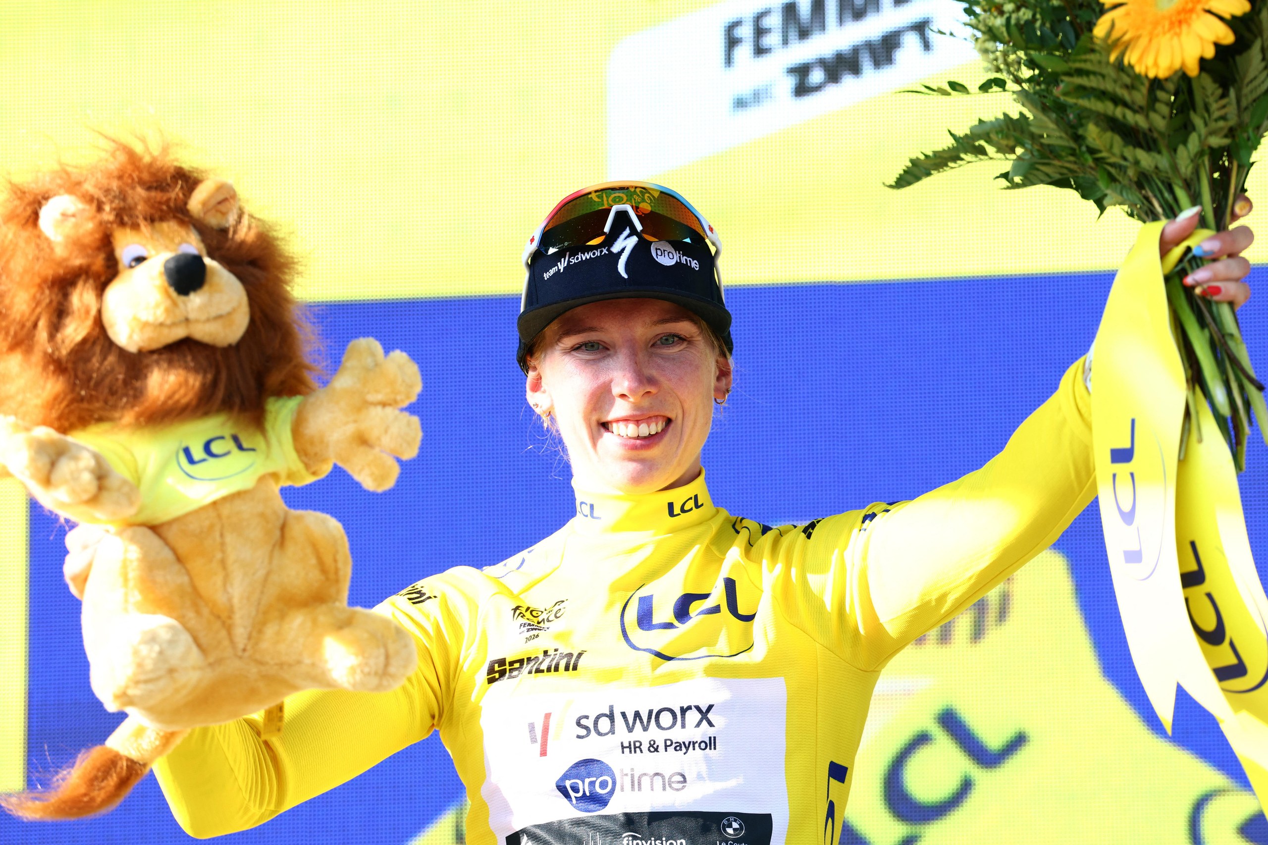 Lorena Wiebes celebrates on the podium wearing the yellow jersey